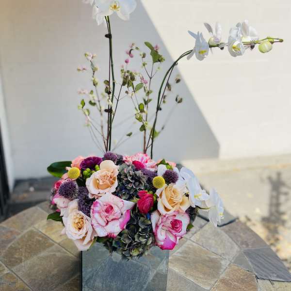 Mixed floral arrangement in a mirrored cube vase with white orchids