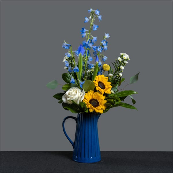 Blue delphiniums and sunflowers in a blue pitcher vase