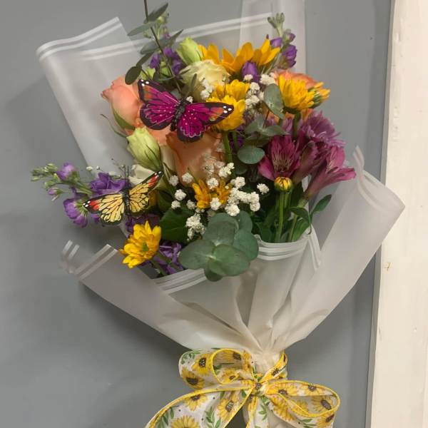 Mixed bouquet of yellow, purple, and peach flowers wrapped in white paper