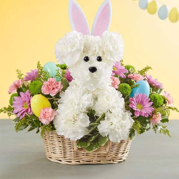 White flower dog in a wicker basket with pastel eggs and bunny ears