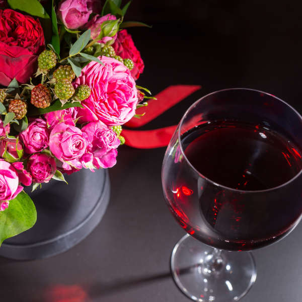 Pink and red rose bouquet beside a glass of red wine