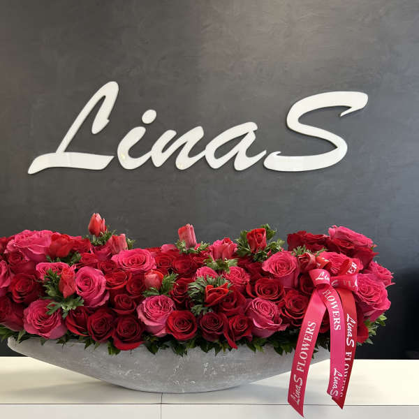 Long arrangement of red and pink roses in a gray container with a pink ribbon