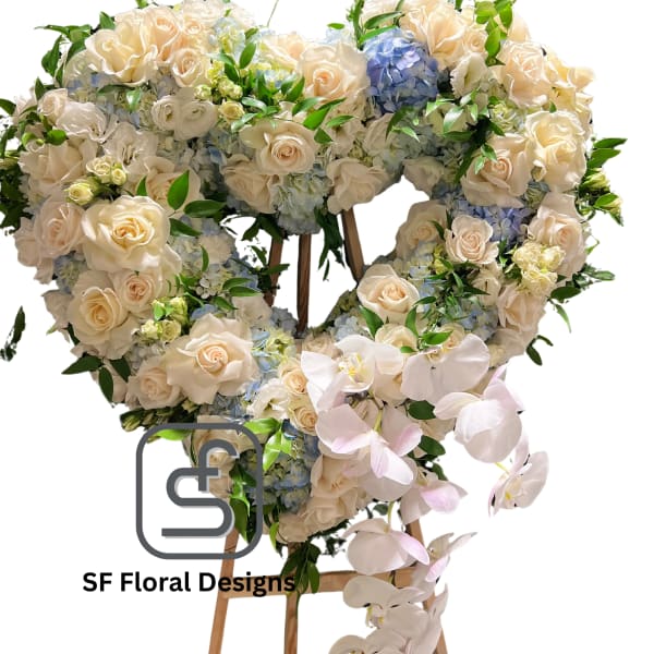 Heart-shaped standing arrangement of cream roses, blue hydrangeas, and cascading white orchids on a wooden easel.