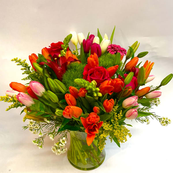 Mixed bouquet of tulips, roses, and a pink gerbera daisy in a glass vase