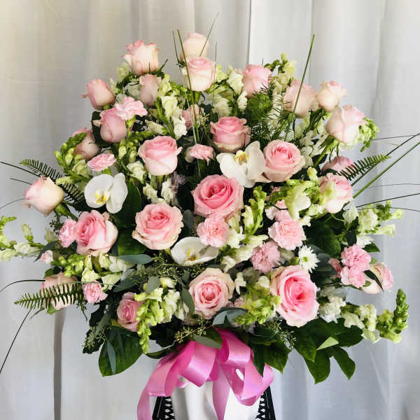 Pink roses and white orchids in a white vase with a pink ribbon