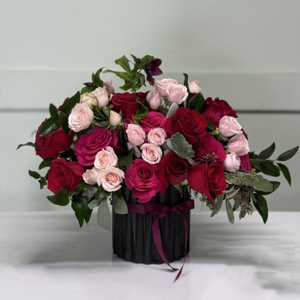Bouquet of red and pink roses in a black vase with ribbon