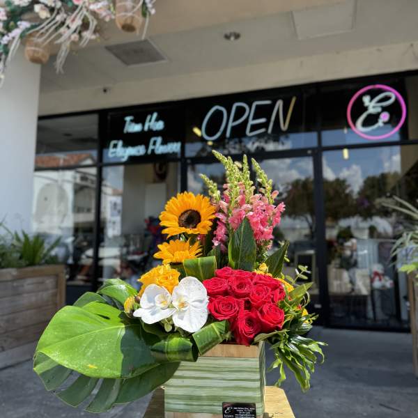 Bright mixed flower arrangement in a wooden box with roses, sunflowers, and orchids