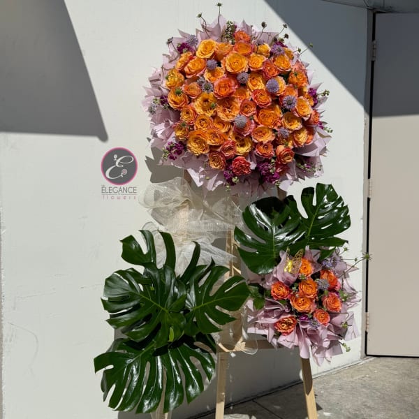 Two floral standing arrangements with orange roses and large tropical leaves on easels
