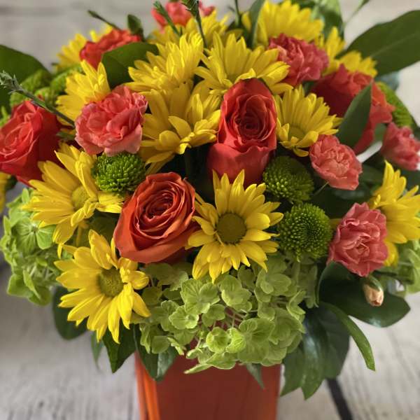 Bouquet of yellow daisies, red roses, and pink carnations in an orange vase