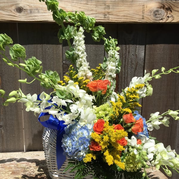 Mixed flower basket with white orchids, orange roses, blue hydrangea, and yellow filler