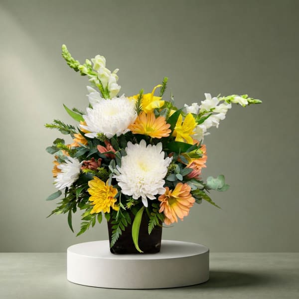 Mixed bouquet of white, yellow, and peach flowers in a dark vase
