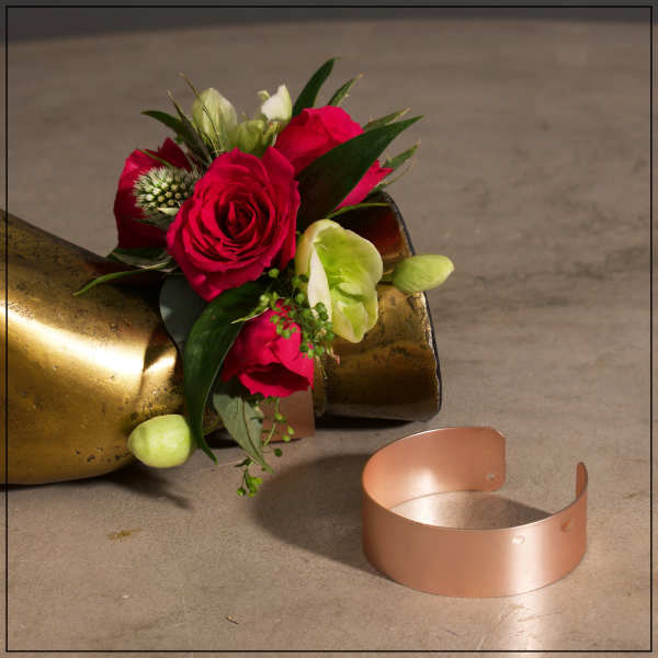 Red rose corsage with pale green accents beside a copper bracelet cuff