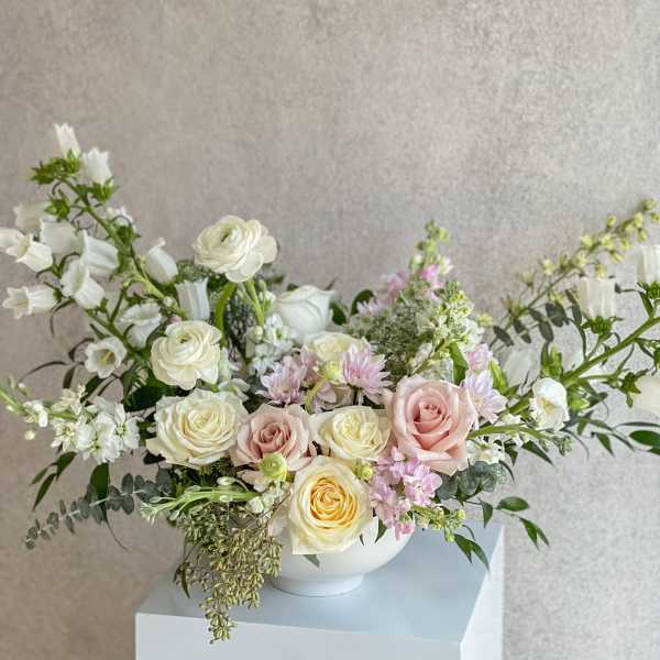 Pastel bouquet of roses and white blooms in a white bowl vase