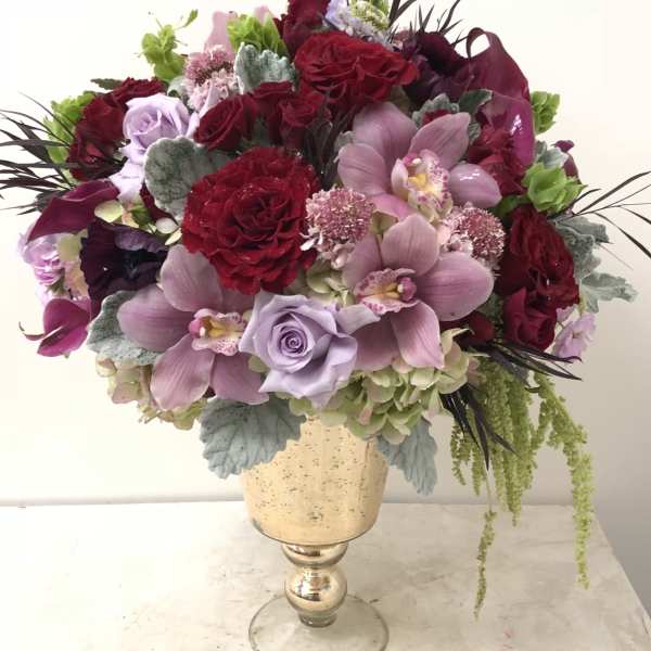 Bouquet of red and lavender flowers in a gold pedestal vase