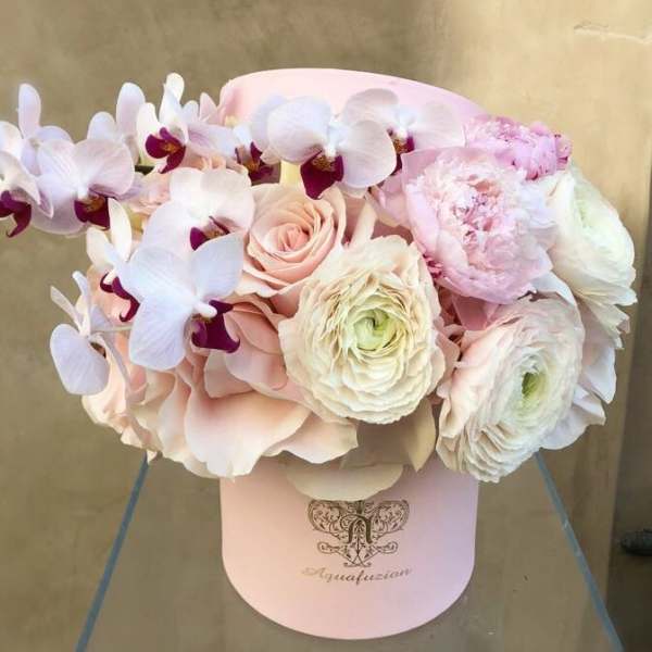 Pastel bouquet of orchids, roses, and ranunculus in a pink hat box