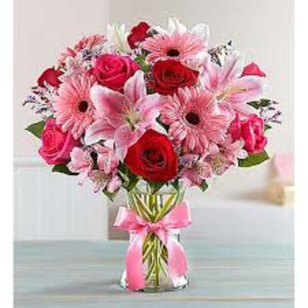 Bouquet of pink and red flowers in a clear glass vase with a pink ribbon