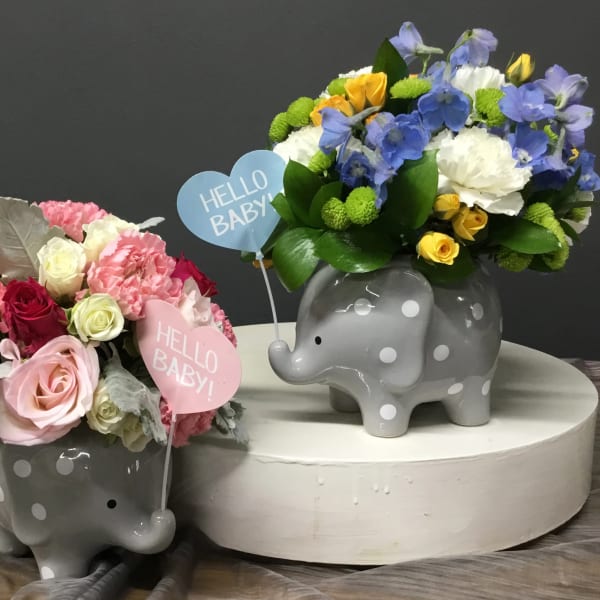 Two polka dot elephant vases filled with mixed pastel flowers and Hello Baby heart picks.
