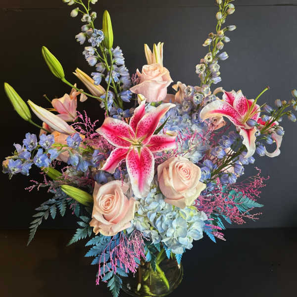 Bouquet of pink lilies, pale roses, and blue flowers in a glass vase