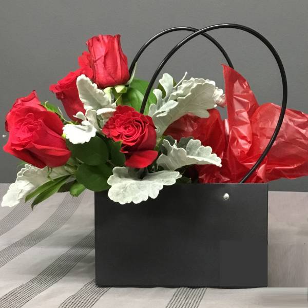 Red roses in a black gift bag with silver foliage and red tissue paper