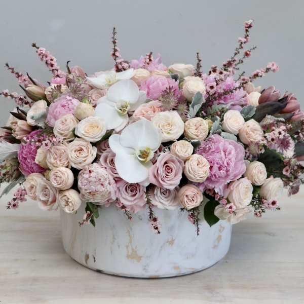 Low arrangement of blush roses, pink peonies, and white orchids in a round white ceramic vase