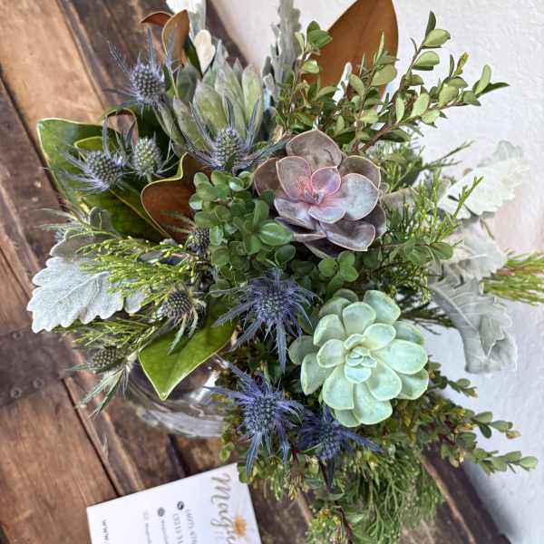 Succulent arrangement with blue thistle-like blooms in a glass vase