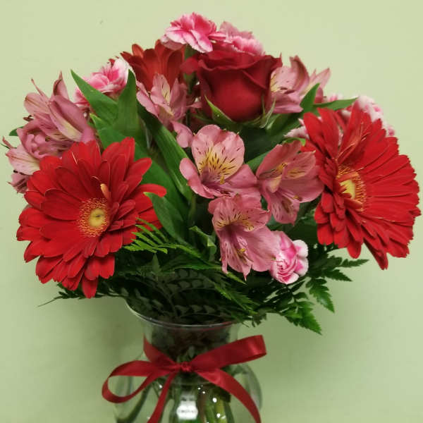 Red gerbera daisies and pink roses in a glass vase with a red ribbon