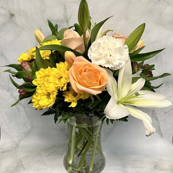 Peach roses, white lilies, and yellow daisies in a glass vase