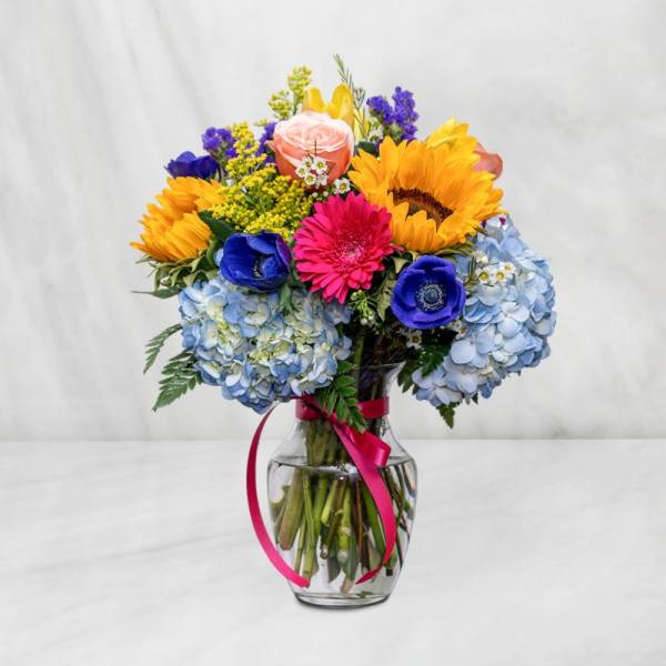 Colorful bouquet of mixed flowers in a glass vase with a pink ribbon