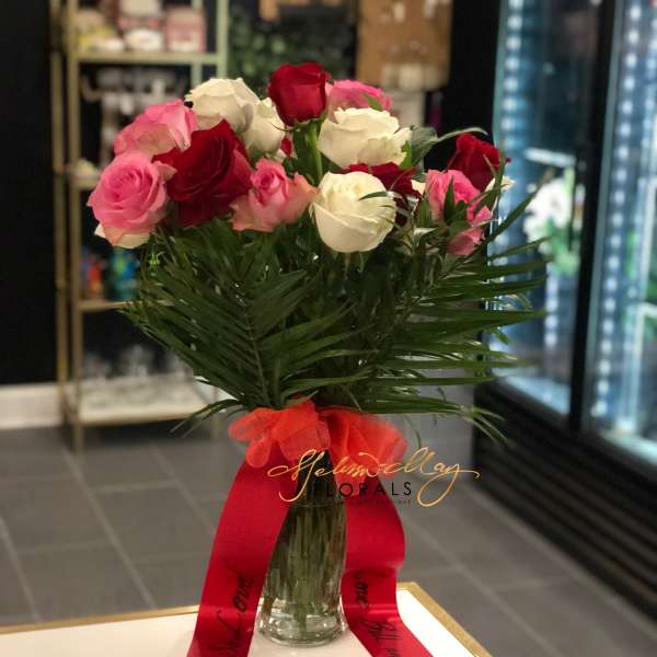 Bouquet of red, pink, and white roses in a glass vase with a red ribbon