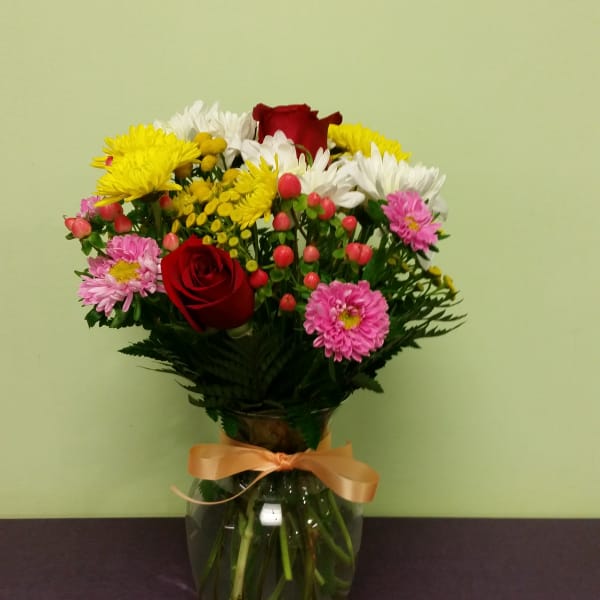 Mixed bouquet of roses and daisies in a glass vase with a ribbon