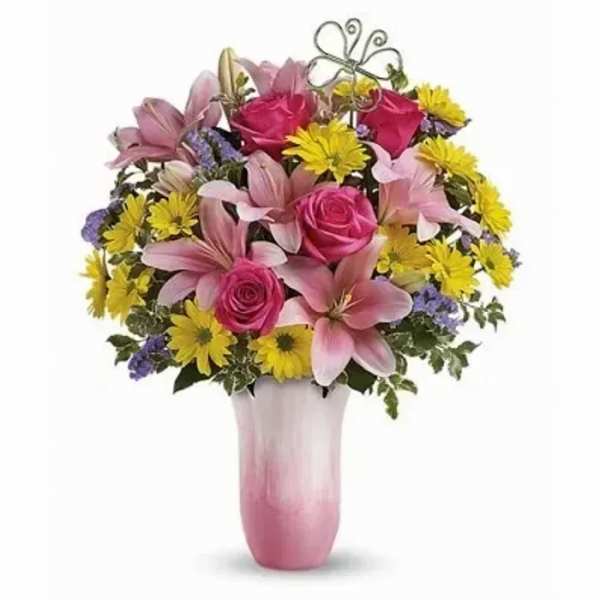 Pink lilies and roses with yellow daisies in a pink and white vase with a small butterfly pick