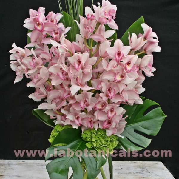 Pink orchid arrangement in a glass vase with large tropical leaves