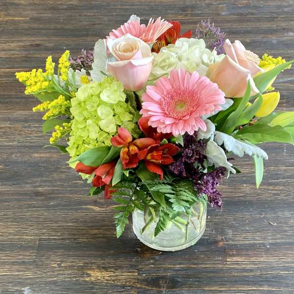 Mixed bouquet of pink roses, gerbera daisies, and hydrangeas in a glass vase
