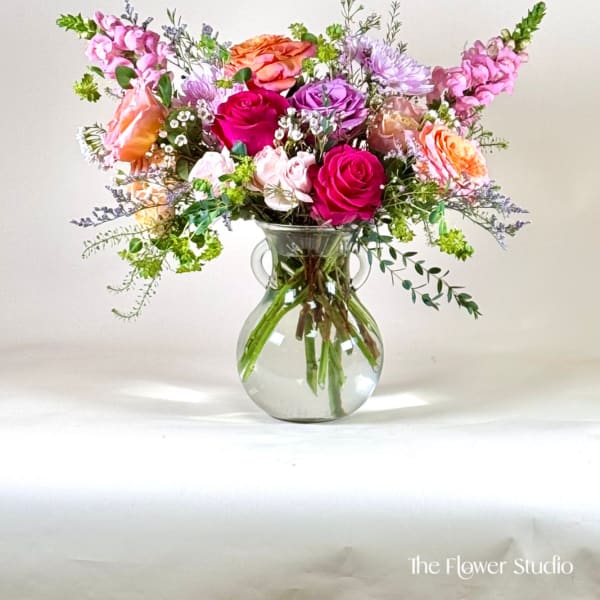Mixed pink, purple, and orange flowers in a clear glass vase
