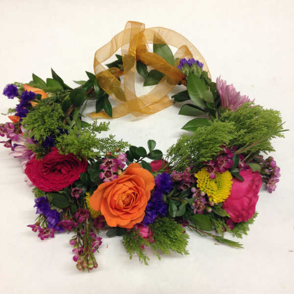 Floral wreath with roses and mixed blooms tied with a gold ribbon