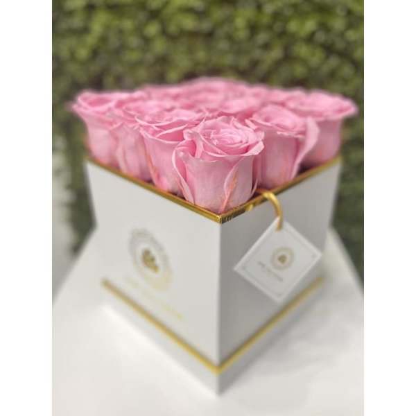 Square white box filled with tightly packed pink roses on a white surface