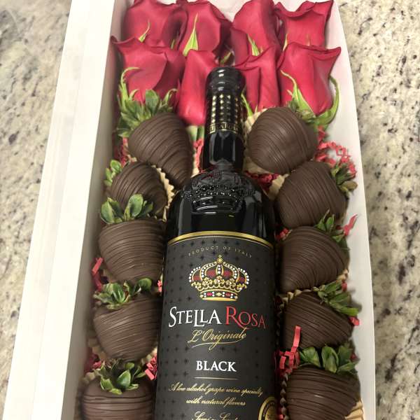 Gift box with red roses, chocolate-covered strawberries, and a wine bottle