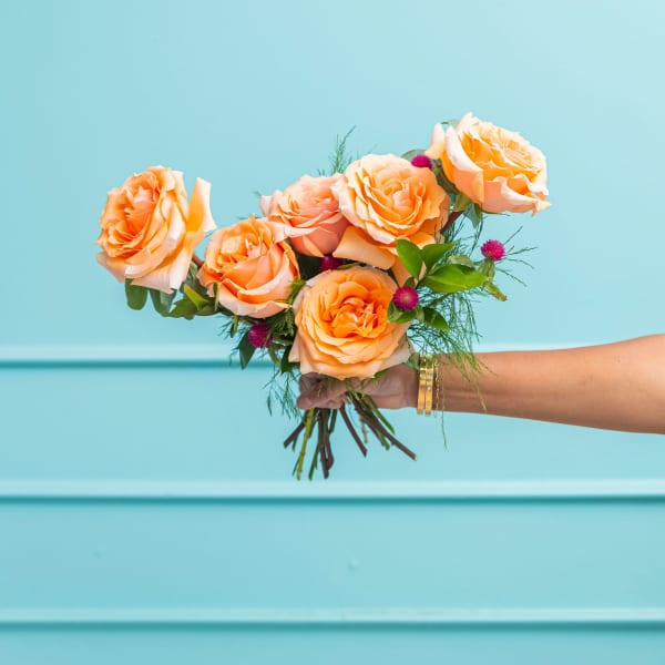 Handheld bouquet of peach roses with small magenta accents