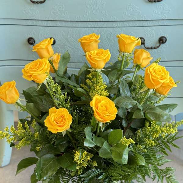 Yellow roses arranged in a clear glass vase with greenery