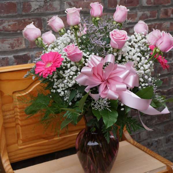 Pink roses and gerbera daisies in a vase with a pink ribbon