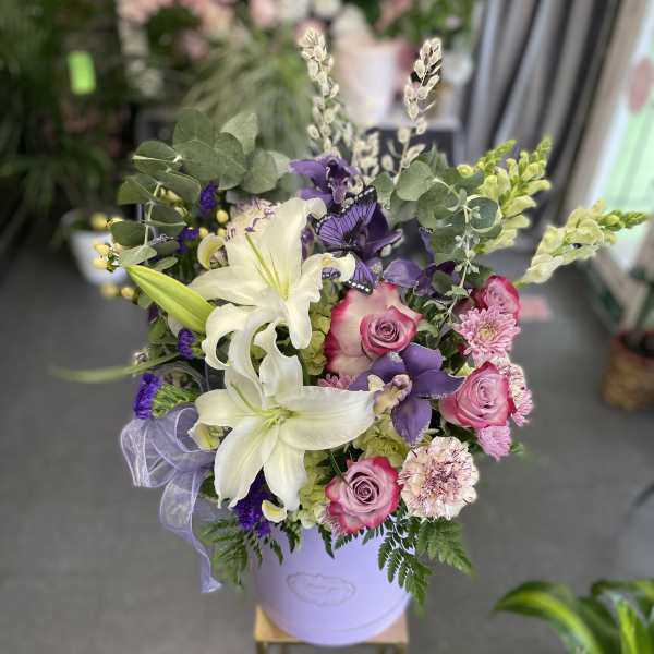 Bouquet of white lilies, pink roses, and purple flowers in a lavender hatbox