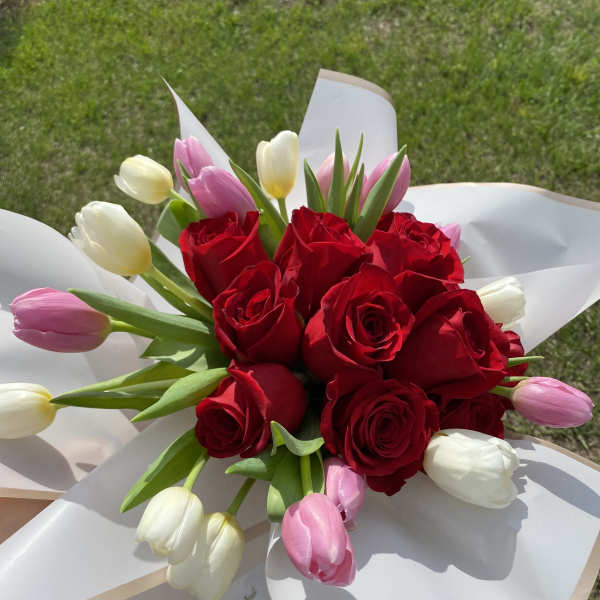 Bouquet of red roses and pink and white tulips wrapped in white paper