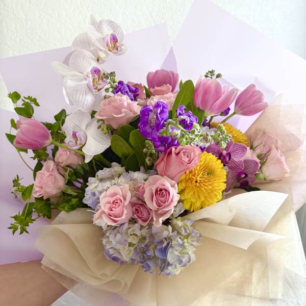 Bouquet of pink roses, tulips, orchids, and yellow mums wrapped in cream paper