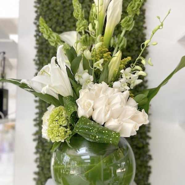White and green flower arrangement with calla lilies and roses in a round glass vase