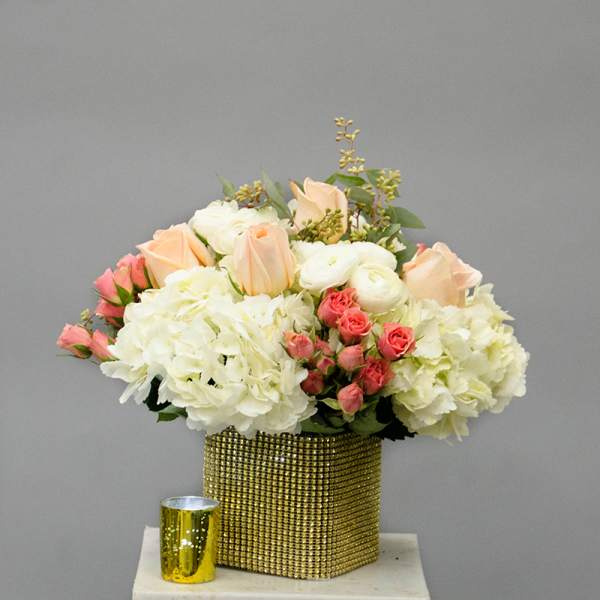 Bouquet of white and peach flowers in a gold square vase