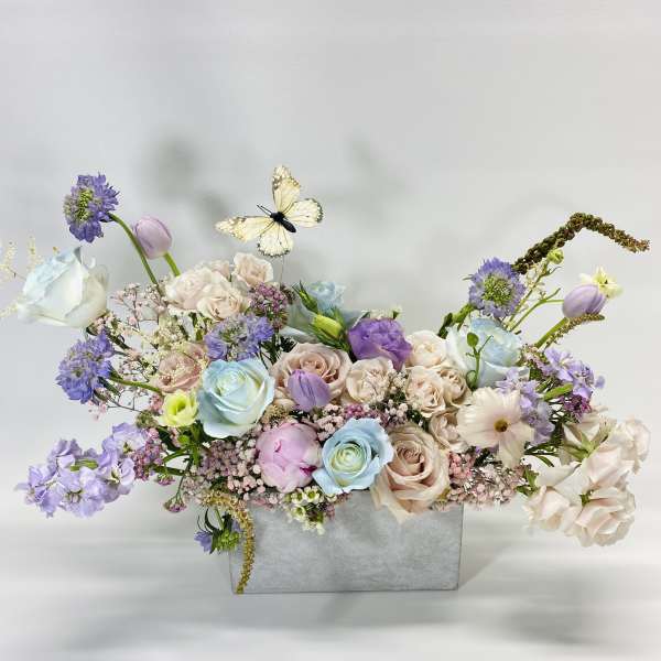 Pastel floral arrangement in a gray box with a butterfly accent