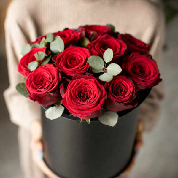 Red roses arranged in a black hatbox with eucalyptus