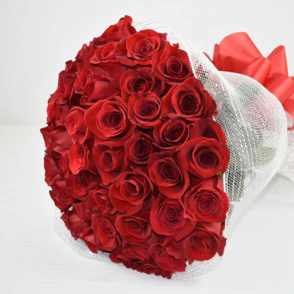 Large bouquet of red roses wrapped in white mesh with a big red bow.