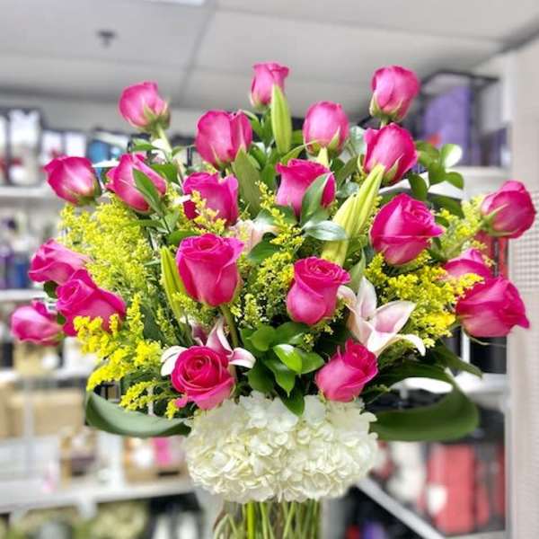 Tall glass vase of hot pink roses, lilies, and white hydrangeas with yellow filler flowers