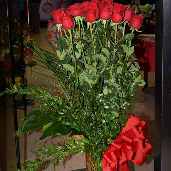Tall bouquet of red roses in a glass vase with a red ribbon
